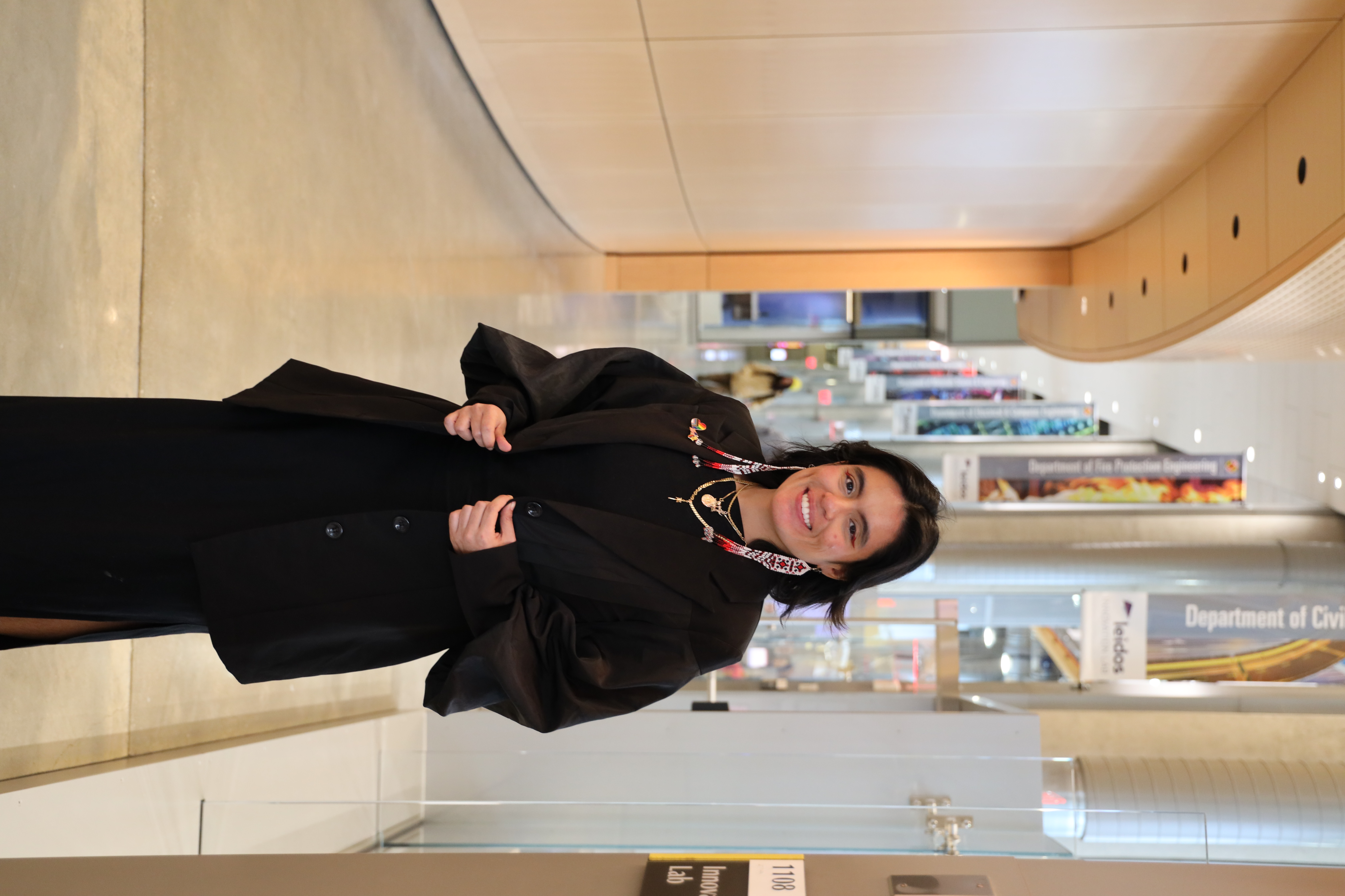 Alison smiling at the camera while standing in a hallway wearing a black regalia