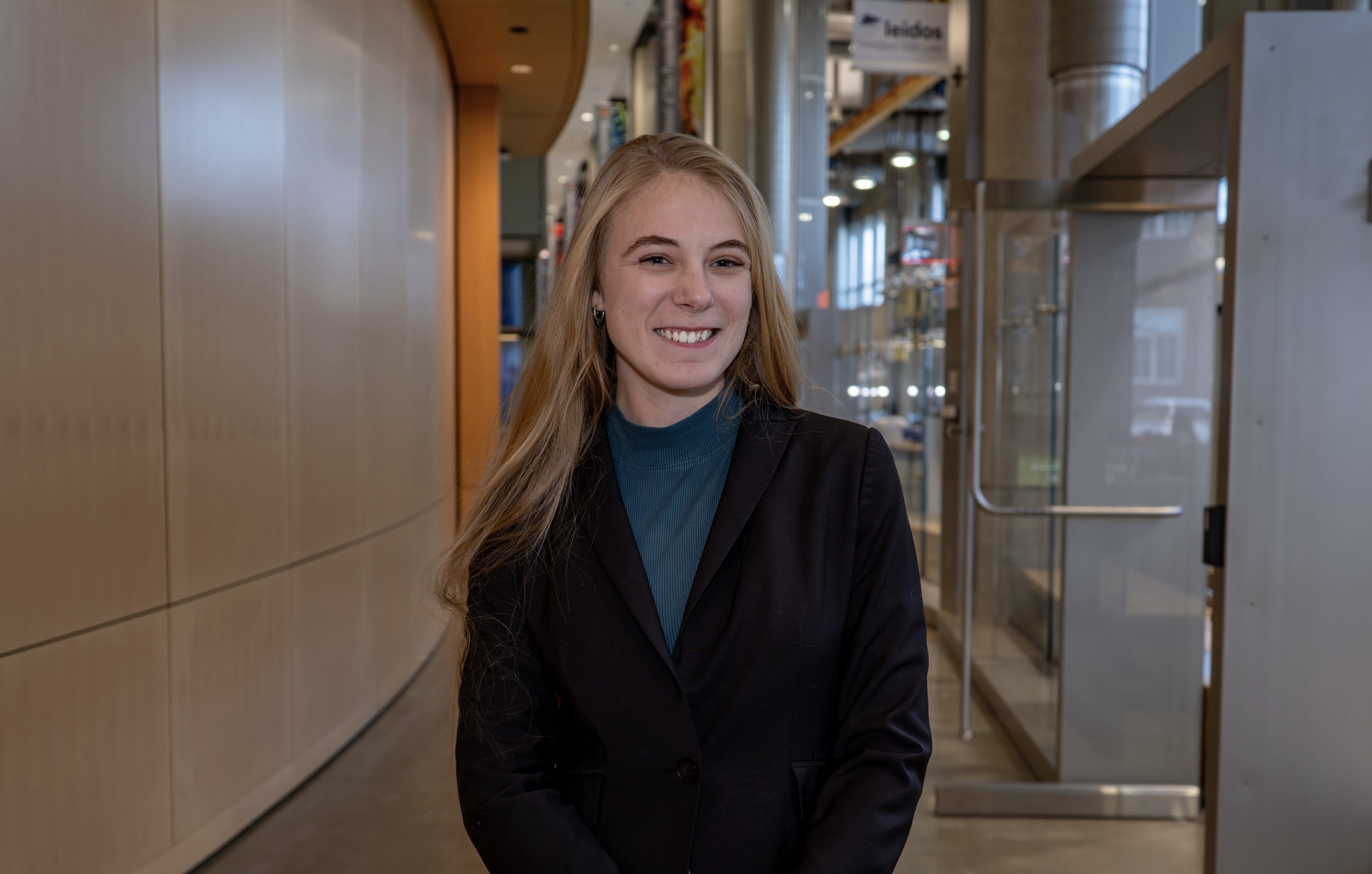 Ashleigh smiling at the camera in a hallway while wearing a dark blazer