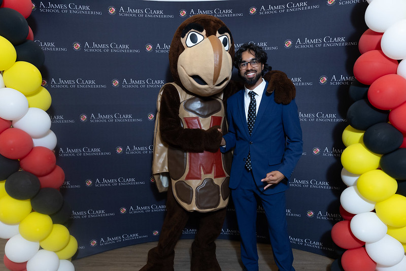 Sulayman Khan poses beside the Testudo mascot at a Clark School of Engineering event, with a branded backdrop and balloons.