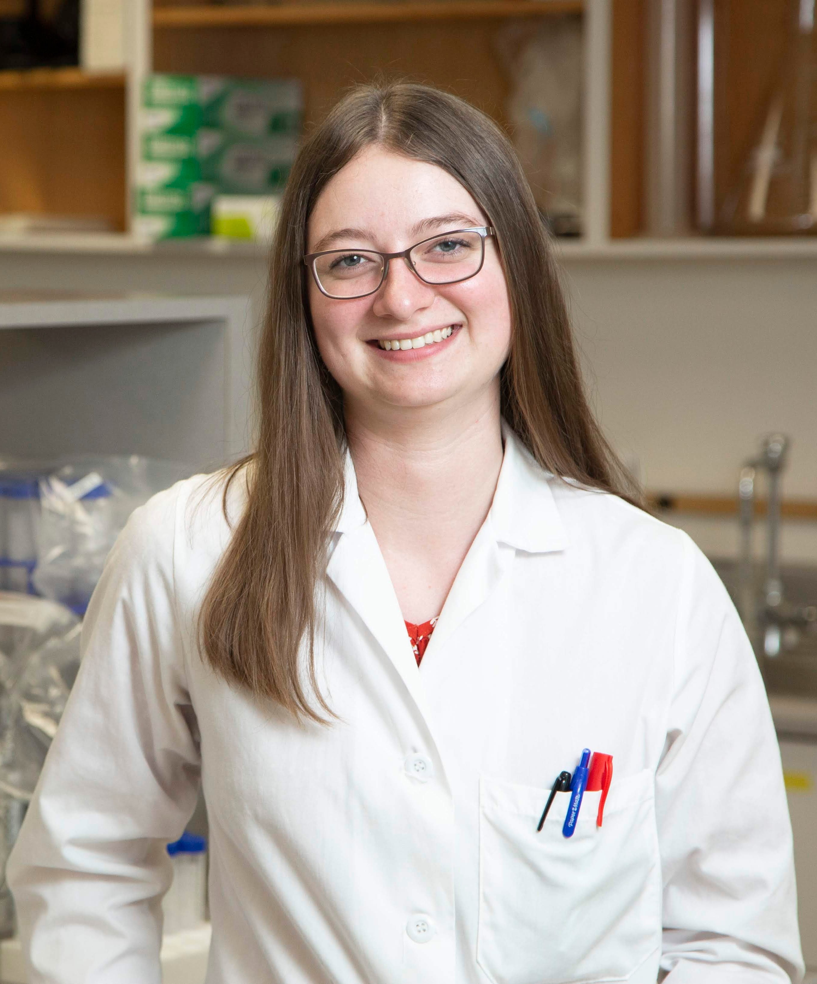 Alexandra smiling at the camera in a white lab coat