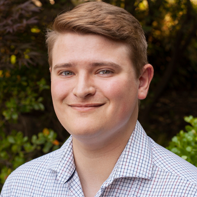 Headshot of Jake Rosvold, smiling in front of foliage