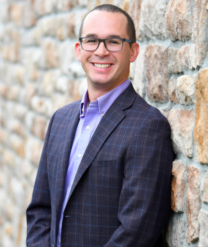 Jarred smiling at the camera outdoors beside a stone wall