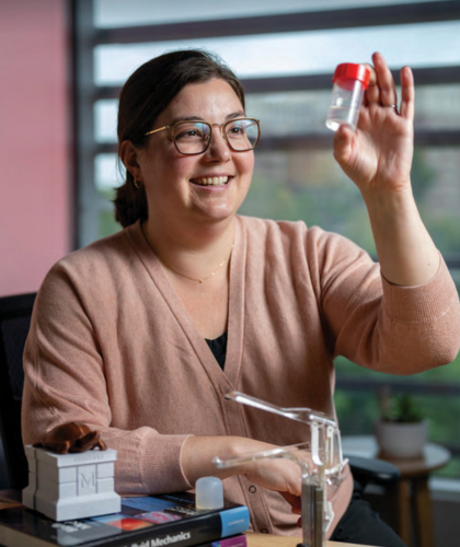 Jenna smiling while holding up a small laboratory sample