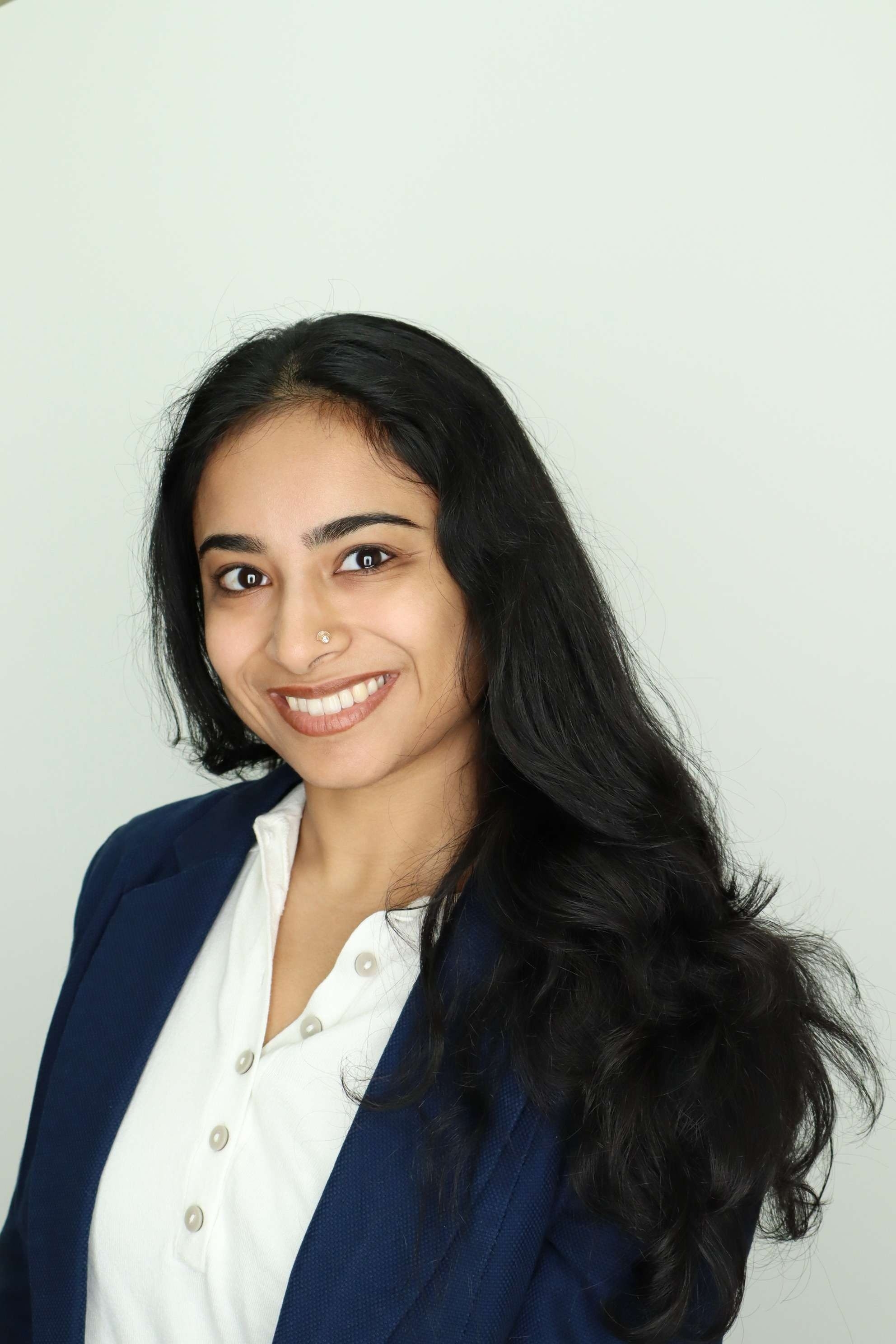 Shohini smiling at the camera while wearing a navy blazer and white blouse